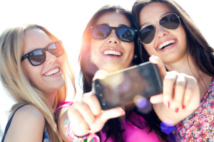 Outdoor portrait of three friends taking photos with a smartphone